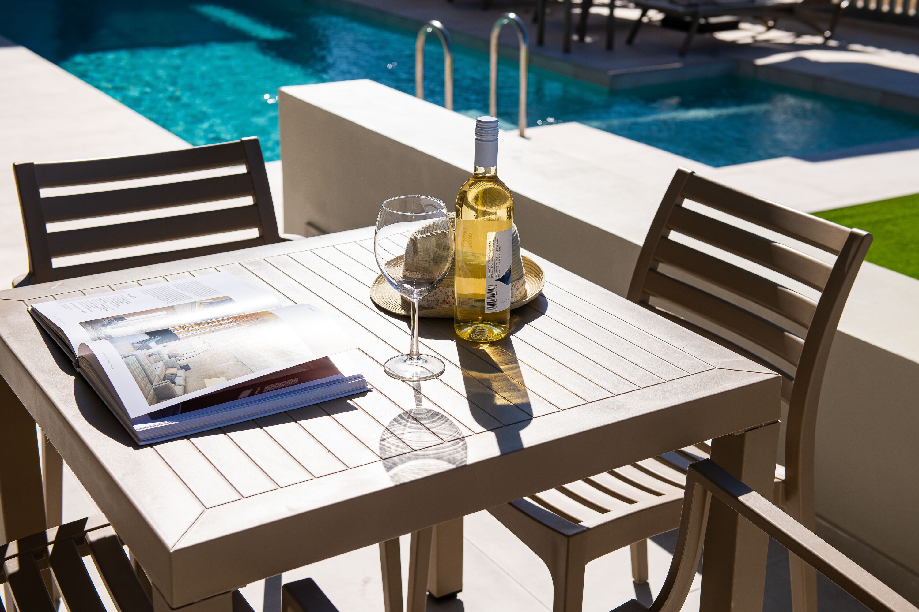 A poolside table with a bottle of white wine, a glass, and a magazine.