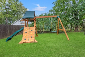 Un’altalena in legno con scivolo e parete da arrampicata in un giardino.