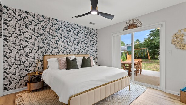Ein Schlafzimmer mit einem Bett, einem Deckenventilator, einem großen Fenster und Blick ins Freie.