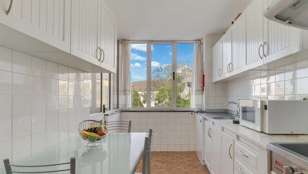 A modern kitchen with white cabinets, a glass dining table, and a view of the outside. - Refugio Madeirense by Atlantic Holiday (Funchal)