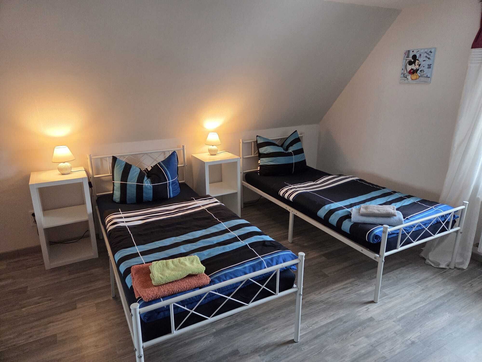 Et soveværelse med to senge, hver med et natbord og en lampe.