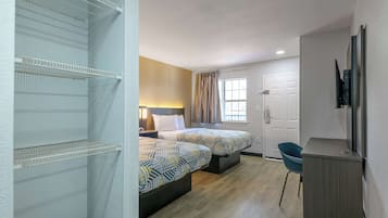 A hotel room with two beds, a desk, a chair, and a TV.