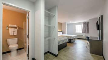 A modern hotel room with a toilet, a bed with patterned bedding, a desk, and a TV.