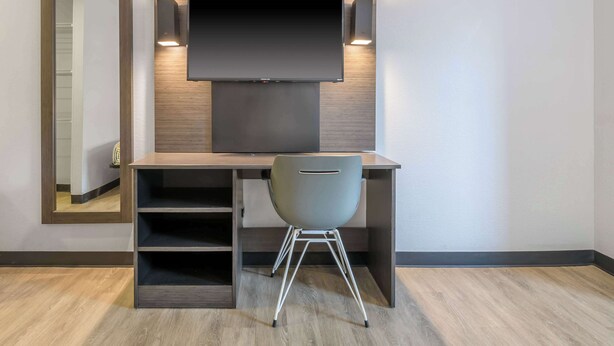 Une chambre moderne avec un bureau en bois, une chaise, un téléviseur fixé au mur et un miroir.