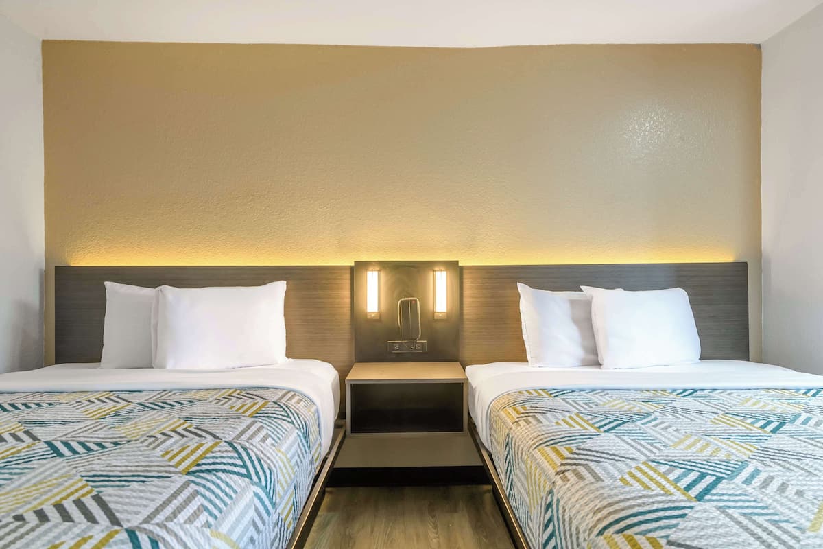 A hotel room with two beds, a nightstand, and a wall-mounted light fixture.