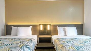A hotel room with two beds, a nightstand, and a wall-mounted light fixture.