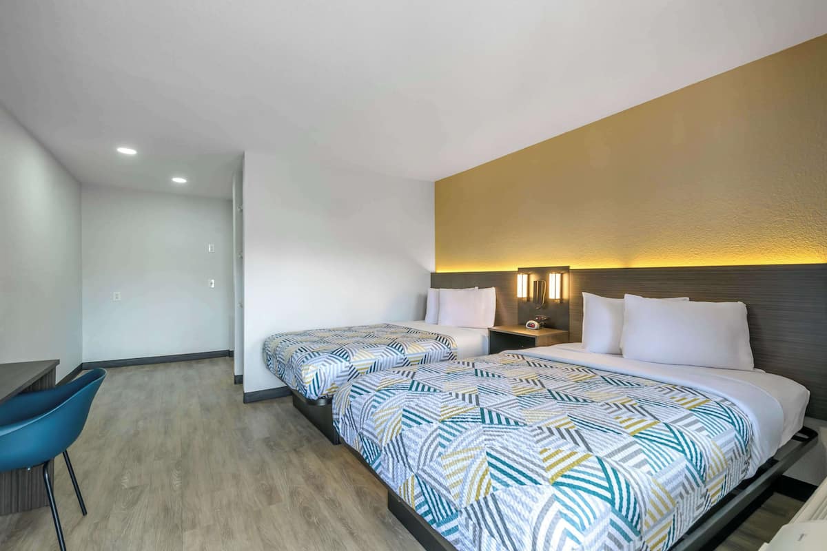 A hotel room with two beds, a desk, and a chair.