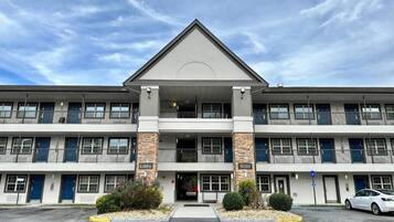 A multi-story hotel with a central entrance, balconies, and a parking lot.