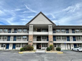 A multi-story hotel with a central entrance, balconies, and a parking lot.