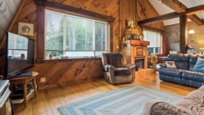 Un interior de cabaña acogedor, con paredes de madera, chimenea, sofá de cuero y televisión.