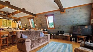 Interior acogedor de una cabaña con techo de madera, un sofá, un televisor y una zona de cocina.