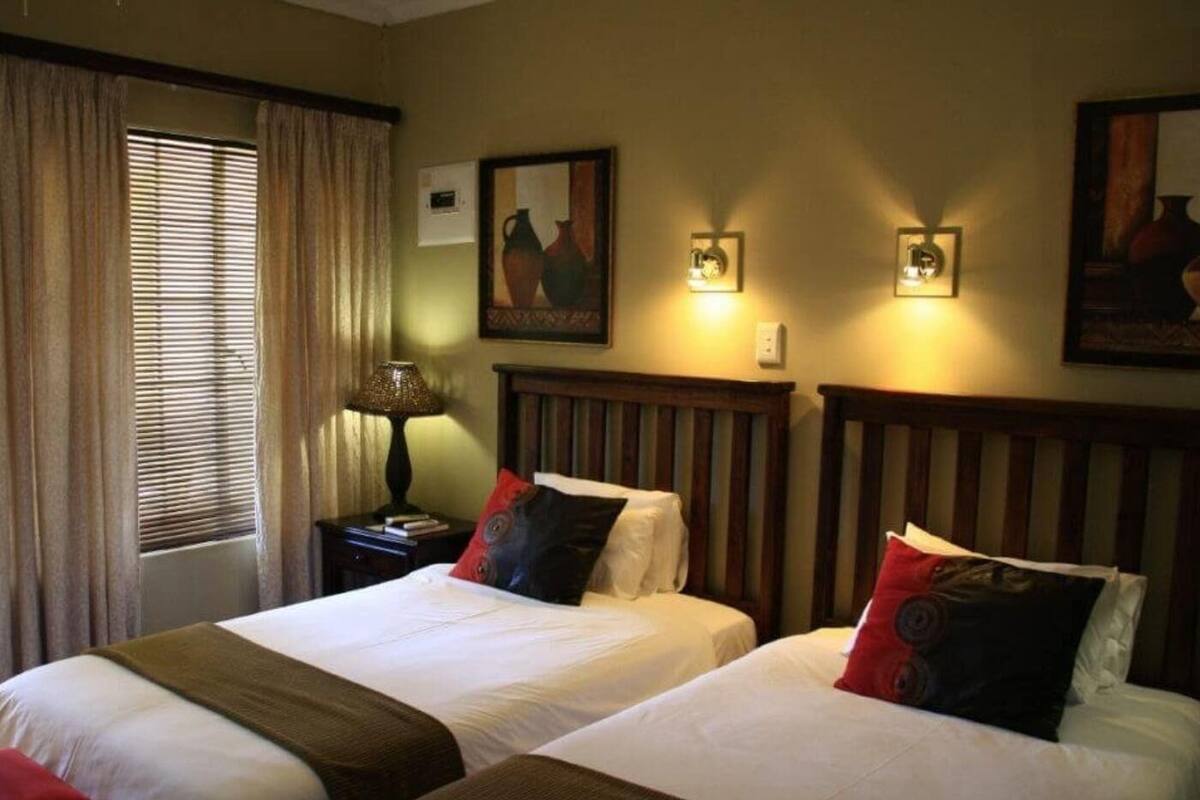 A hotel room with two beds, a nightstand, a lamp, and a window with curtains.
