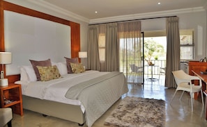 A bedroom with a large bed, two bedside tables, a desk with a chair, and a balcony with a table and chairs.