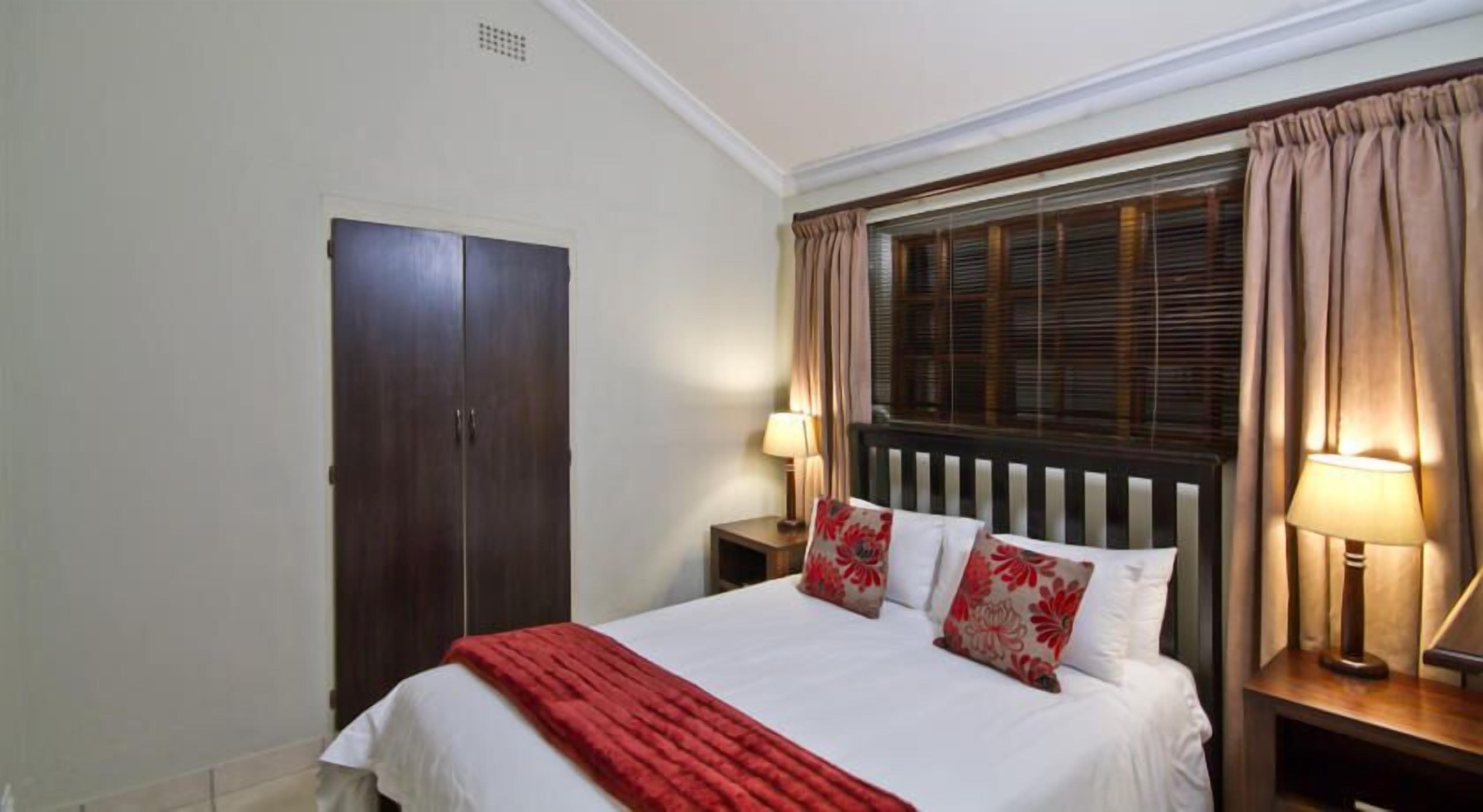 A bedroom with a bed, a wardrobe, two bedside lamps, and a window with curtains.