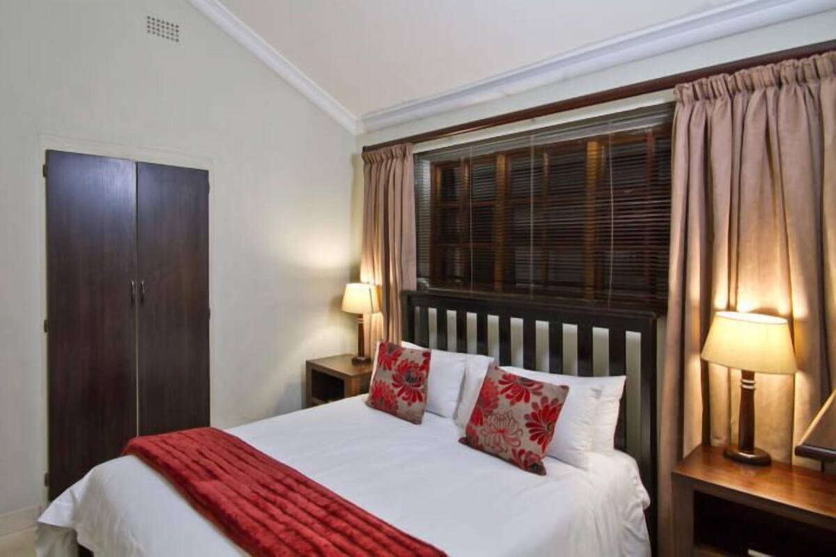 A bedroom with a bed, a wardrobe, two bedside lamps, and a window with curtains.