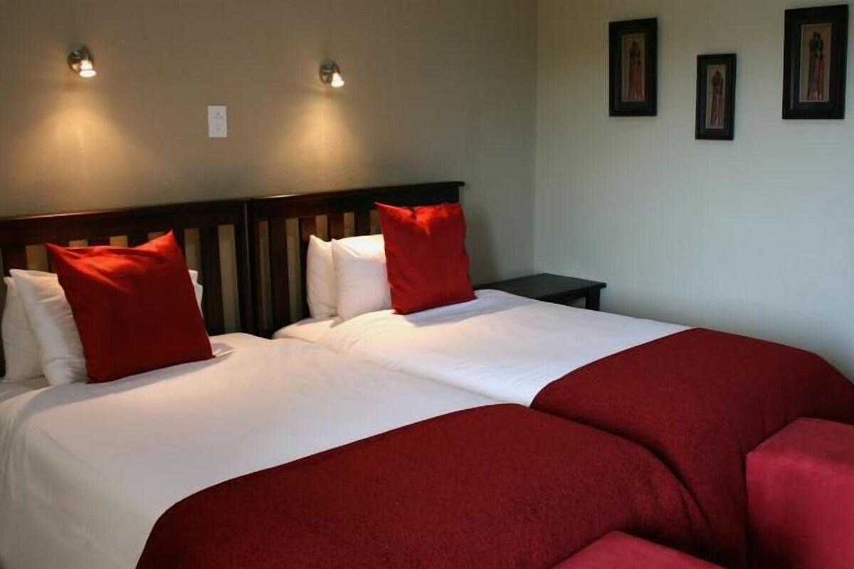 Ein Doppelbett mit roter und weißer Bettwäsche, zwei Wandleuchten und drei gerahmte Bilder an der Wand.