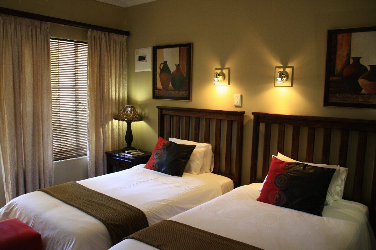 A hotel room with two beds, a nightstand, a lamp, and wall-mounted lights.