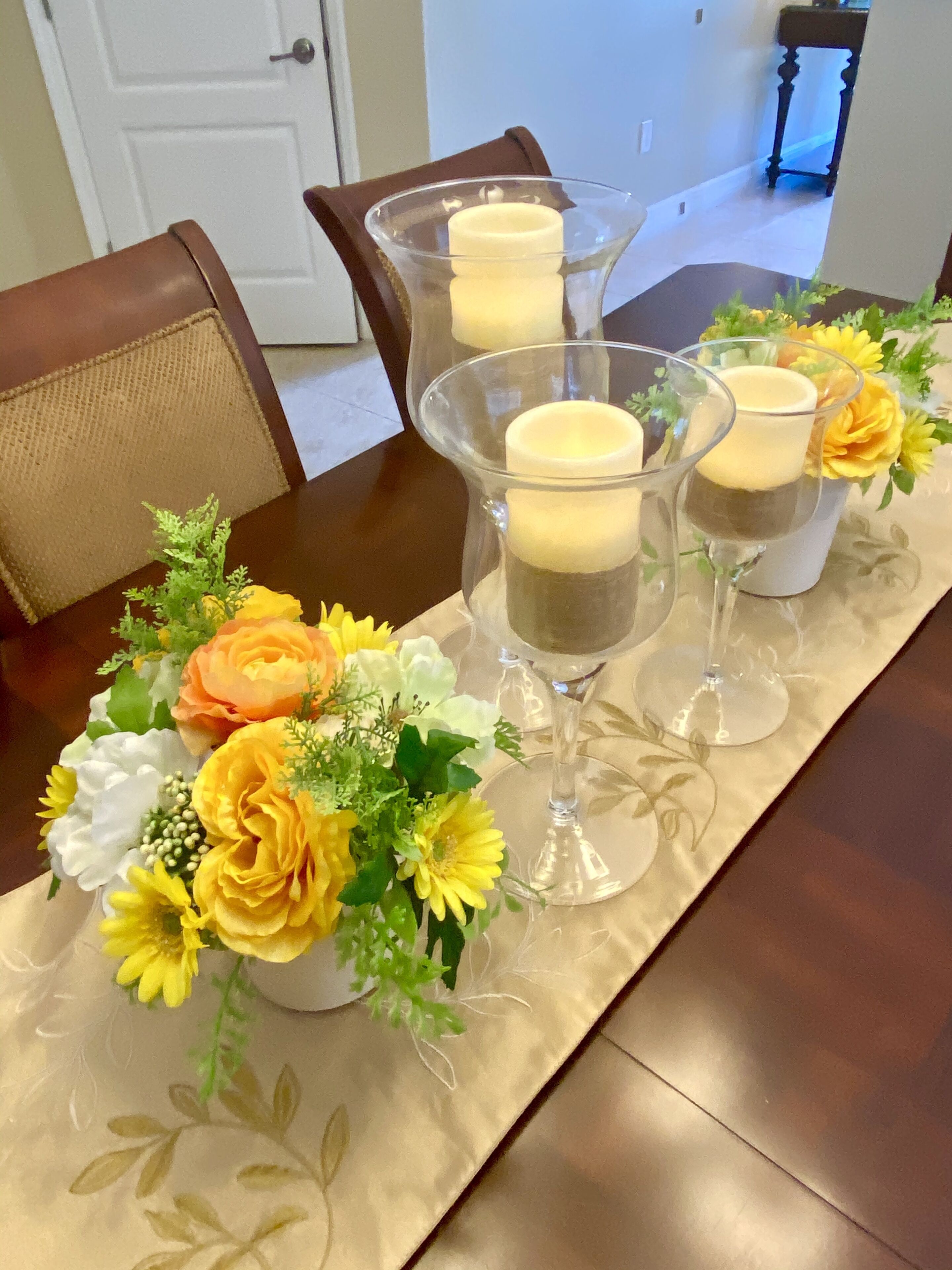 A dining table set with clear glass candle holders containing candles, surrounded by floral centerpieces.