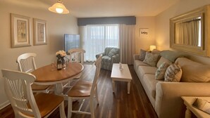 Een woonkamer met een ronde houten tafel, witte stoelen, een bank en een televisie.