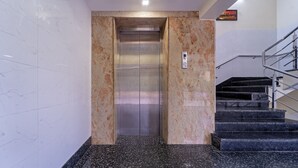 An elevator with a marble wall, a metal handrail, and a staircase with black steps. - Itsy Hotels Sri Mani'S Residency, Coimbatore Airport (Coimbatore)