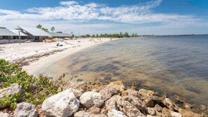 Una playa con agua cristalina, una orilla arenosa y un edificio con techo.