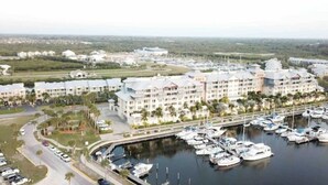 Un puerto deportivo con varias embarcaciones amarradas, rodeado por un complejo turístico con varios edificios y una carretera que conduce al puerto.