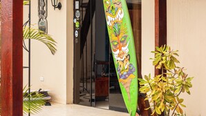A building entrance with a green decorative flag, a wooden balcony, and a potted plant. - Hospedaje Sueños DE Chicama, MAS Cerca AL Point, CON UNA Vista Expectacular (LA LIBERTAD)