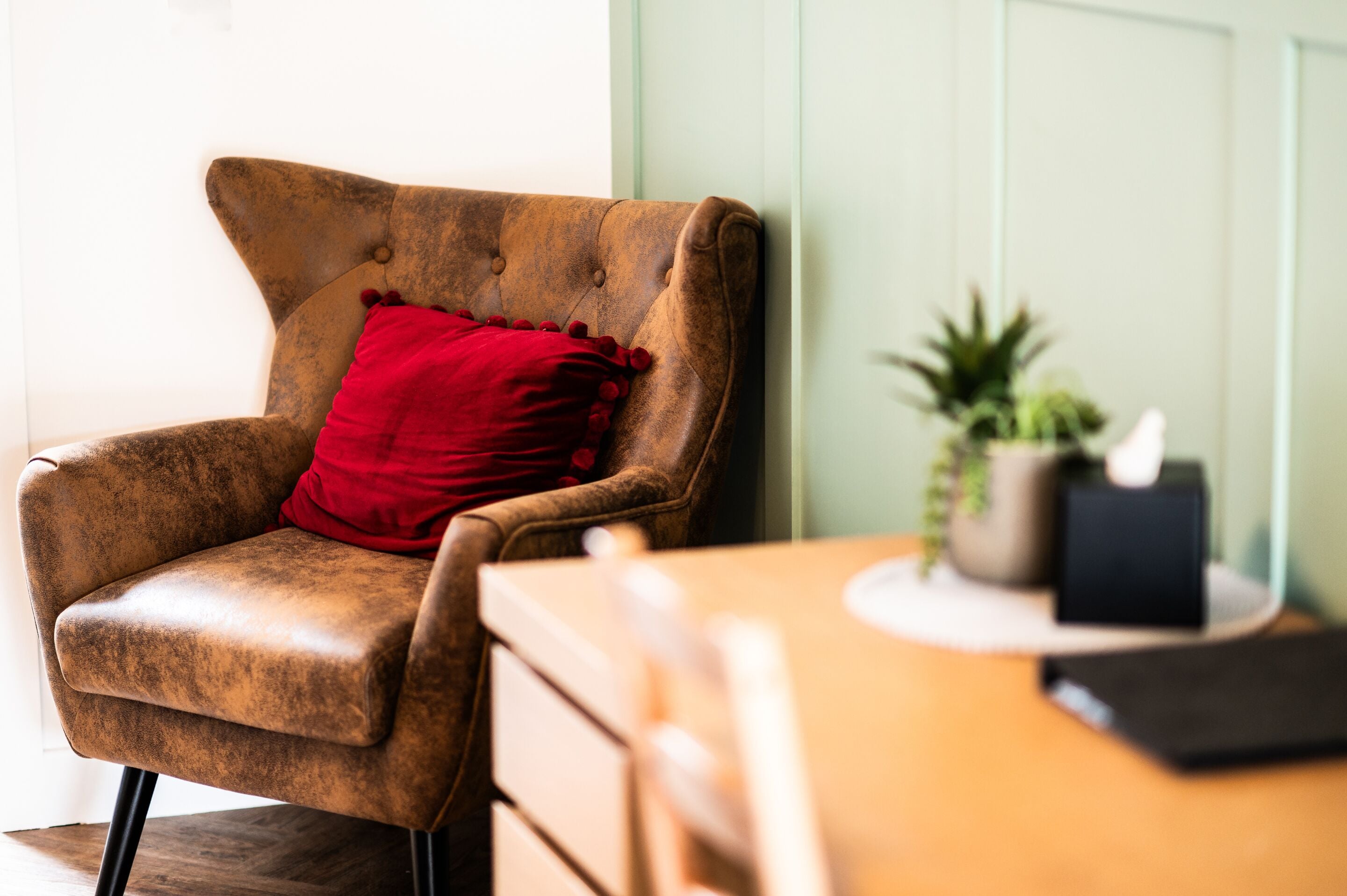 A brown leather armchair with a red pillow, a wooden table, a small potted plant, and a black box.