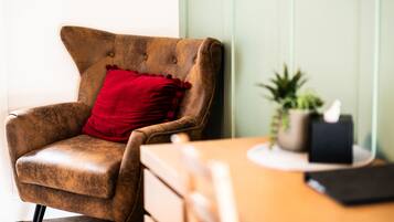 A brown leather armchair with a red pillow, a wooden table, a small potted plant, and a black box.