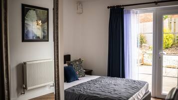 A bedroom with a bed, a radiator, a nightstand, a pillow, a curtain, and a door leading to an outdoor area.