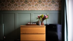 A wooden dresser with drawers, a vase with flowers, and a black appliance in a room with patterned wallpaper and a radiator. - Stonehenge Courtyard (Salisbury)