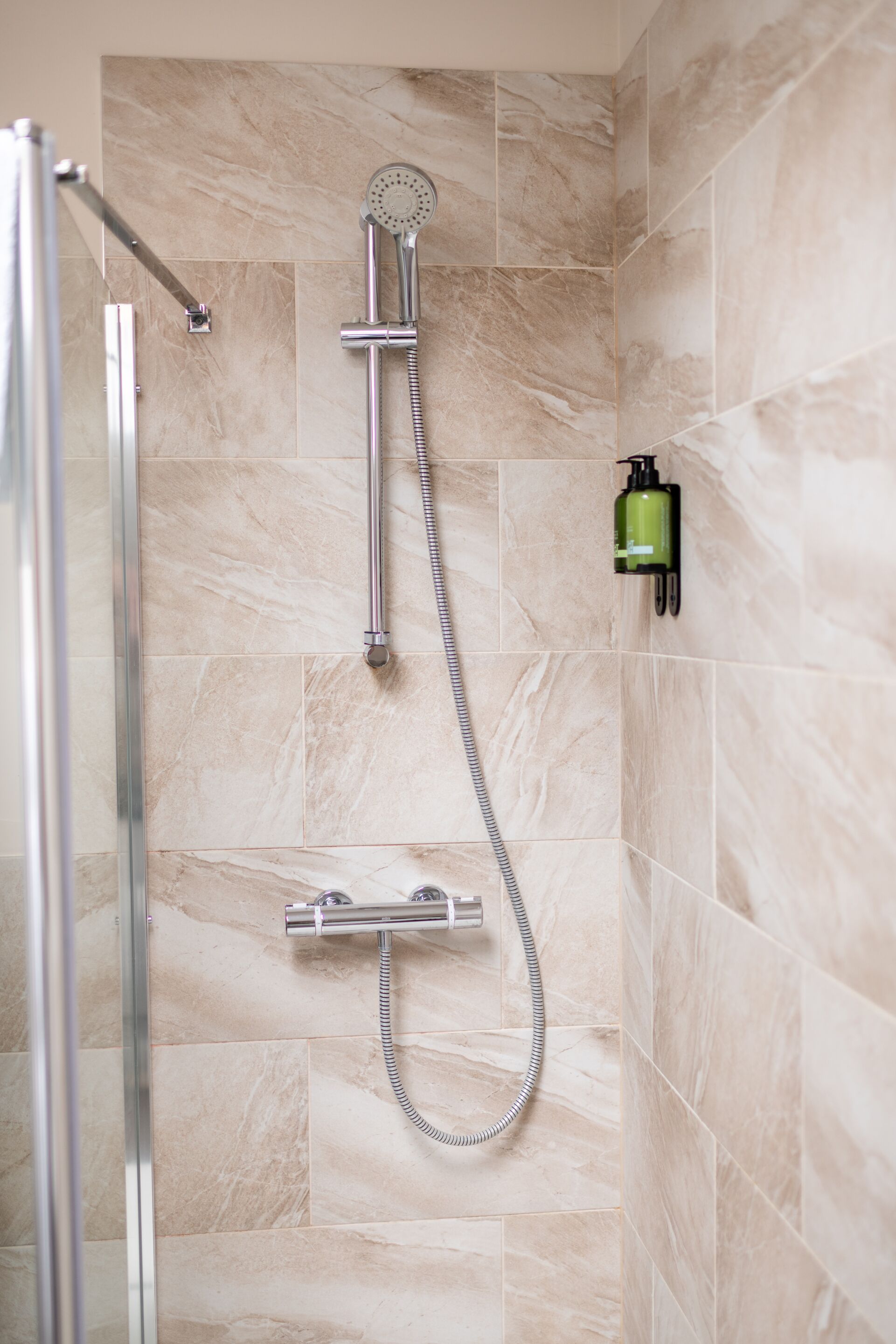 A shower with a handheld showerhead and a wall-mounted faucet.