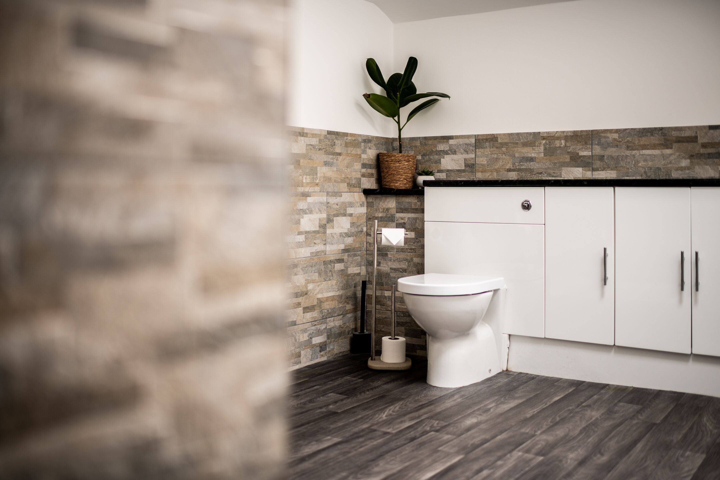 Une salle de bain moderne avec un mur recouvert de pierres, des toilettes blanches et un plancher en bois.