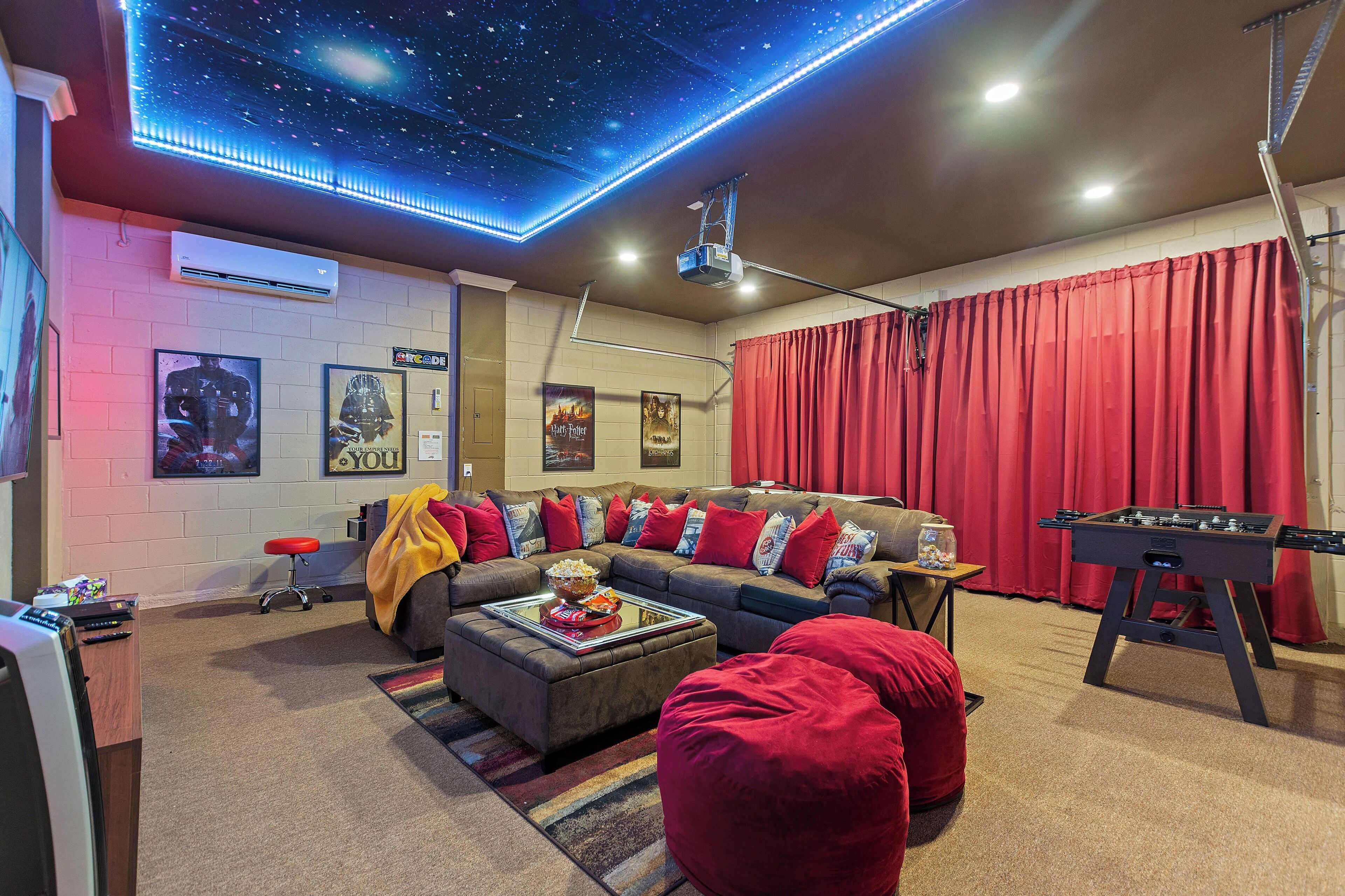 Una sala de estar acogedora con un sofá modular, detalles en rojo, una mesa de fútbol y un techo con estrellas.