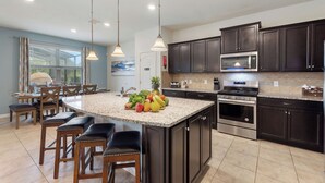 A modern kitchen with dark cabinetry, stainless steel appliances, and a central island with a fruit bowl.