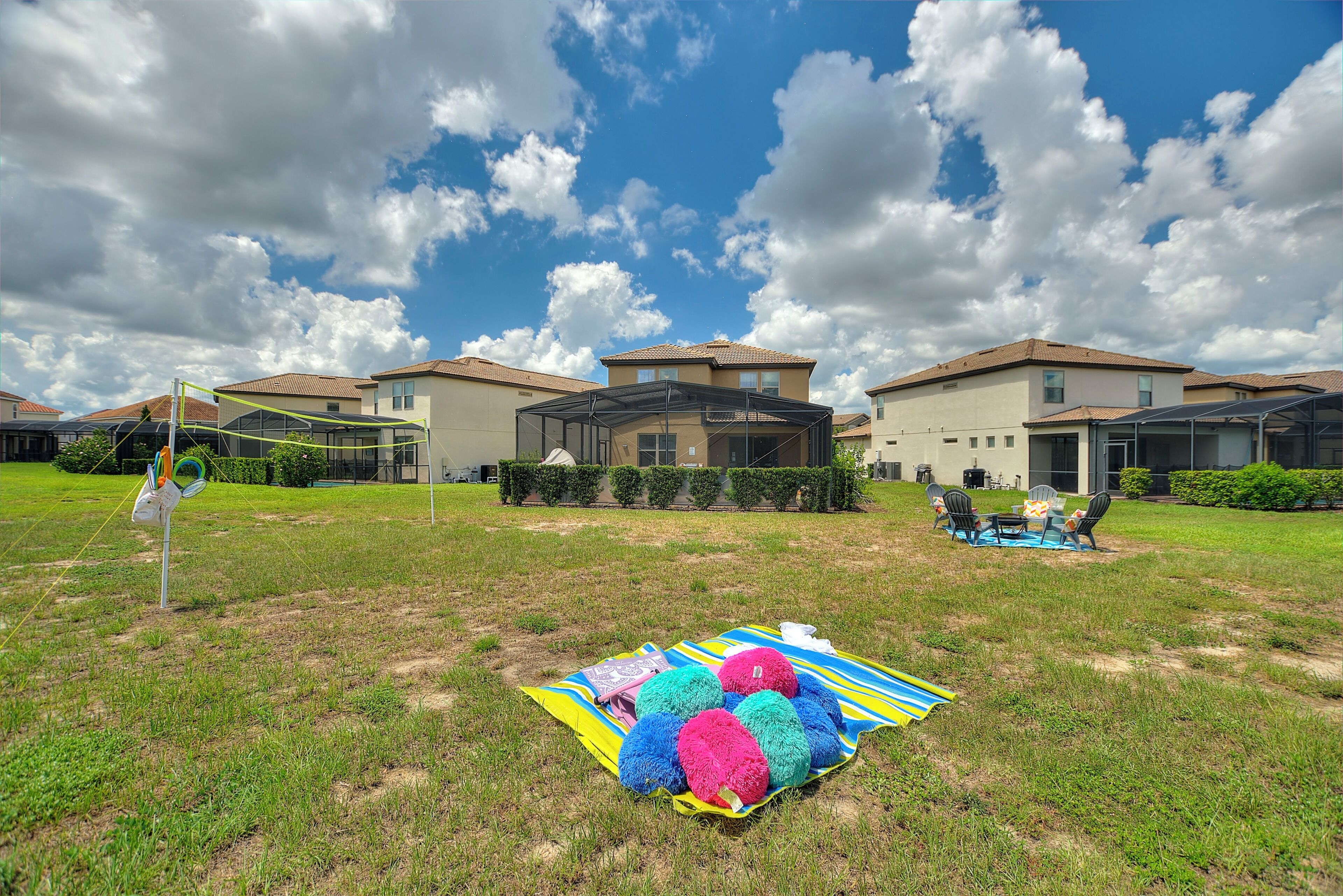 A grassy outdoor area with a picnic setup, including a blanket and colorful balls, in front of a residential building with a covered patio.