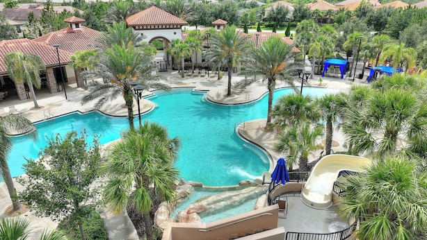 A resort with a large central pool, palm trees, and a slide.