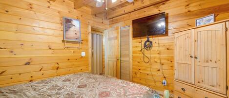 Habitación de cabaña de madera con cama, ventilador de techo, televisor montado en la pared y armario.