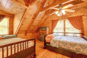 Un dormitorio de cabaña de madera con dos camas, un ventilador de techo y un aparador.
