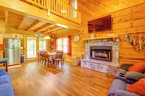 A cabin interior with a dining area, kitchen, living room, and a stone fireplace. - Cabin w/ Hot Tub + Fishing Pond in Del Rio! (Del Rio)