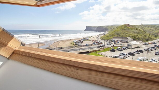 A view from a window overlooking a beach with a parking lot and a building with a flat roof. - Host Stay Burnsyde Beach House (Saltburn-by-the-Sea)