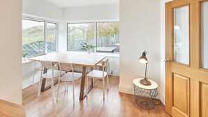 A modern dining area with a wooden table and chairs, large windows, and a lamp. - Host Stay Burnsyde Beach House (Saltburn-by-the-Sea)
