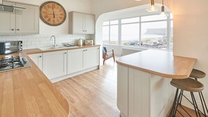 A modern kitchen with white cabinetry, a wooden countertop, and a large window offering a view of the sea. - Host Stay Burnsyde Beach House (Saltburn-by-the-Sea)