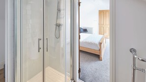 A glass-enclosed shower with a handheld showerhead, a wooden door, and a view into a bedroom with a bed and a nightstand. - Host Stay Burnsyde Beach House (Saltburn-by-the-Sea)