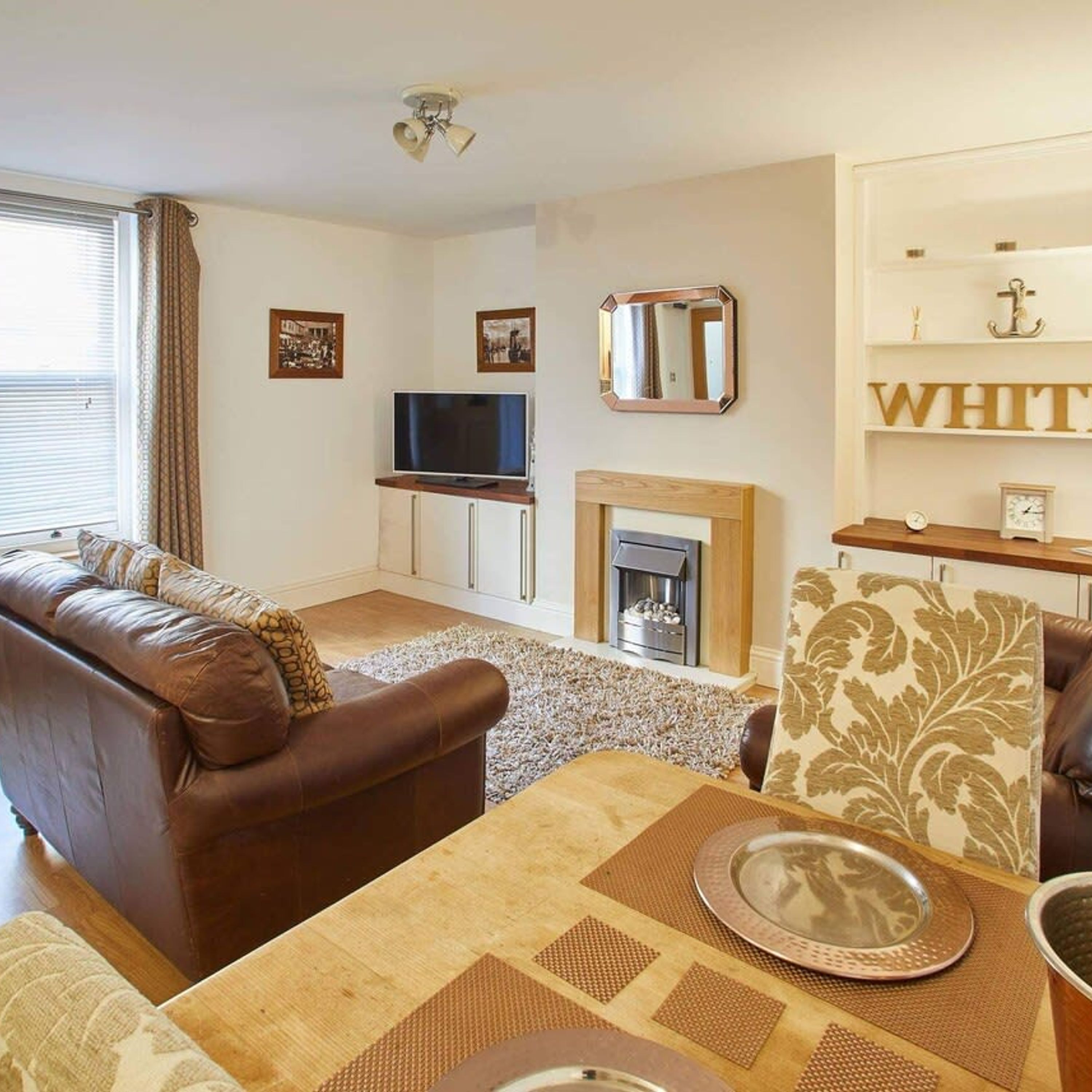 A living room with a brown leather sofa, a television, a fireplace, and a dining table with placemats.