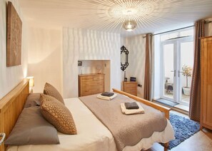 Een slaapkamer met een bed, een houten dressoir en een groot raam met gordijnen.