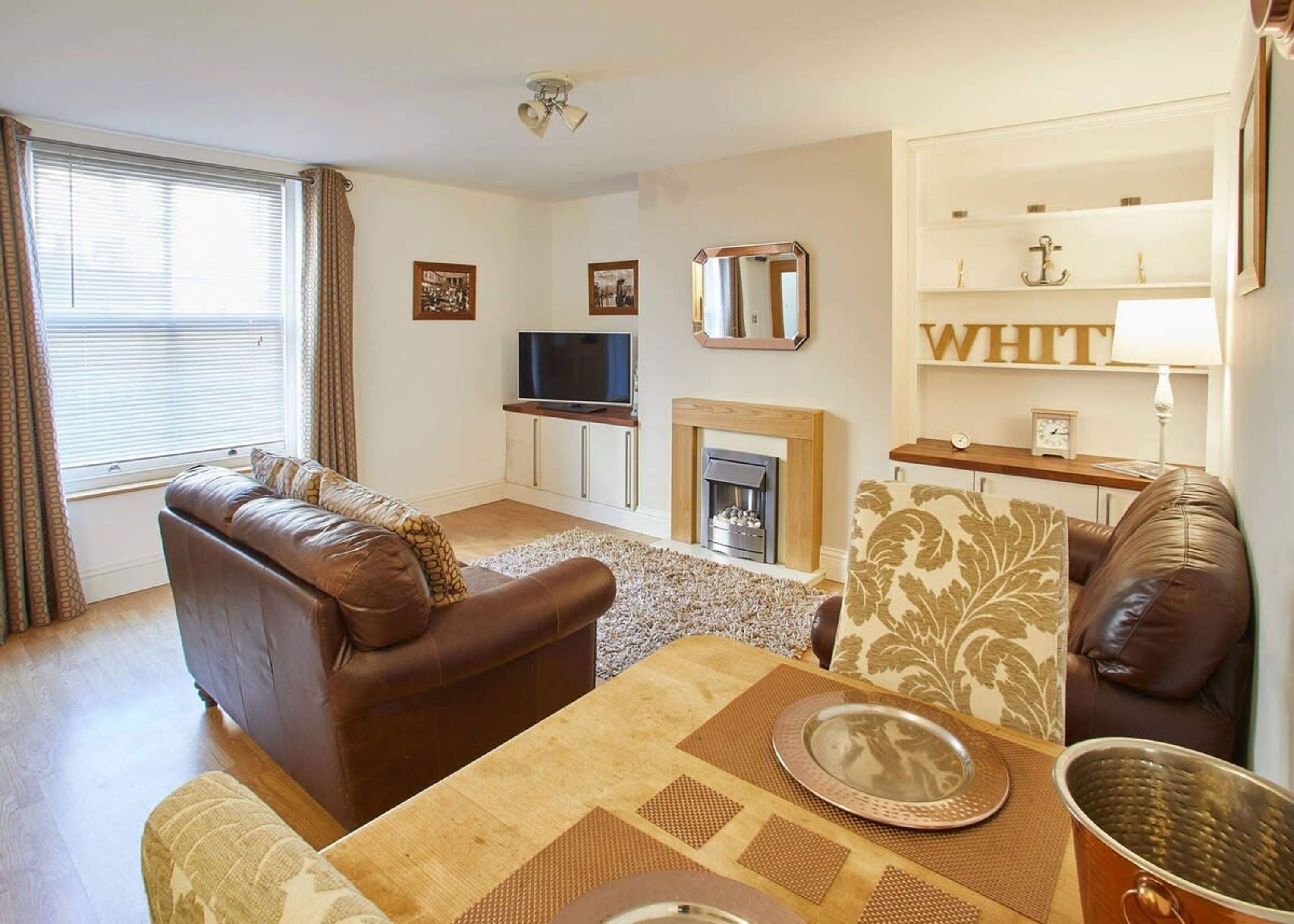 A living room with a brown leather sofa, a television, a fireplace, and a table set with a placemat and a metal bowl.