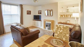 A living room with a brown leather sofa, a television, a fireplace, and a table set with a placemat and a metal bowl.
