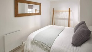 A bedroom with a bed, a wooden-framed mirror, a radiator, and a window with a sheer curtain. - Host Stay Park View Apartment (Whitby)