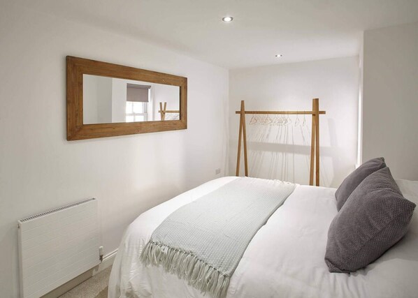 A bedroom with a bed, a wooden-framed mirror, a radiator, and a window with a sheer curtain. - Host Stay Park View Apartment (Whitby)